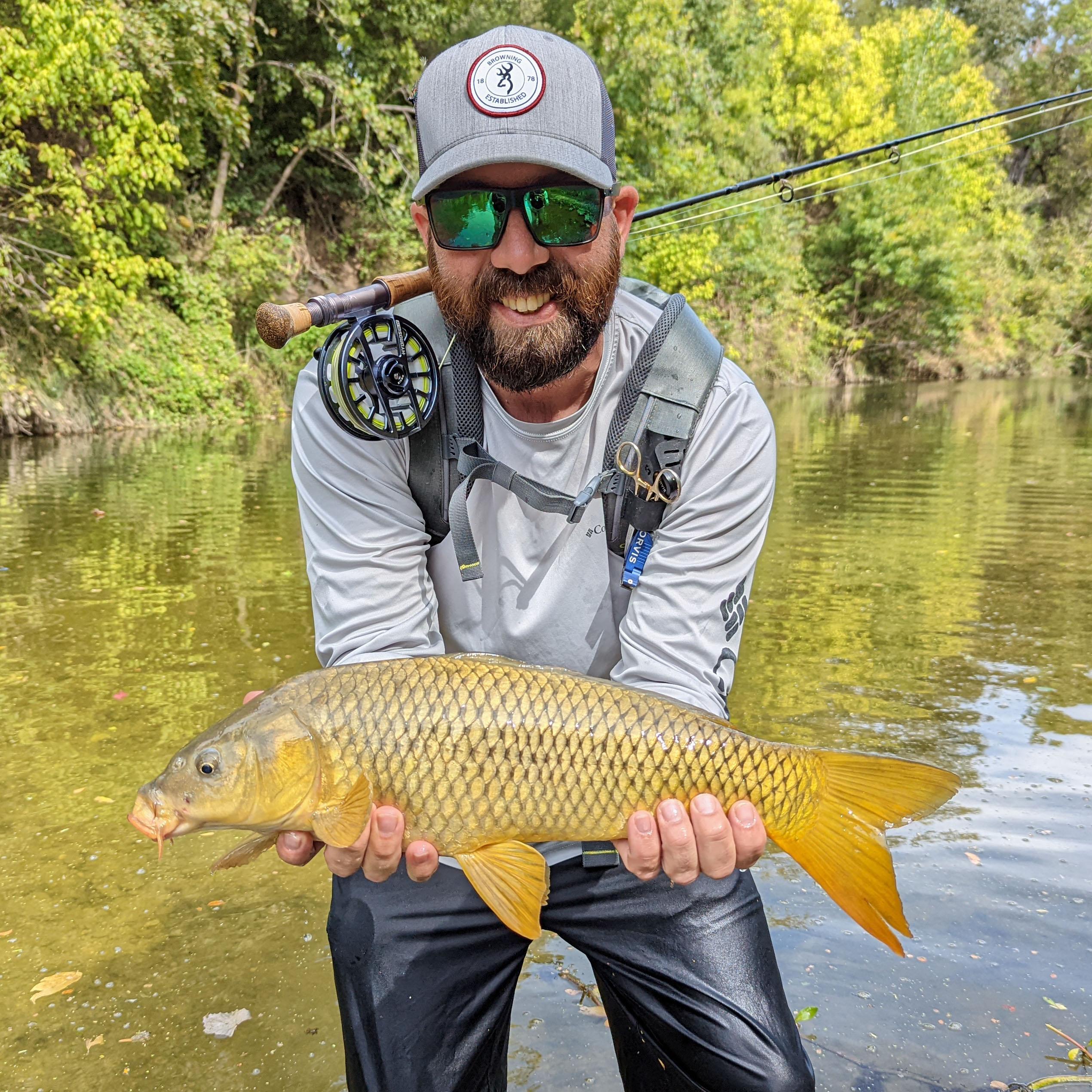Kevin holding a small common carp, standing in a river.